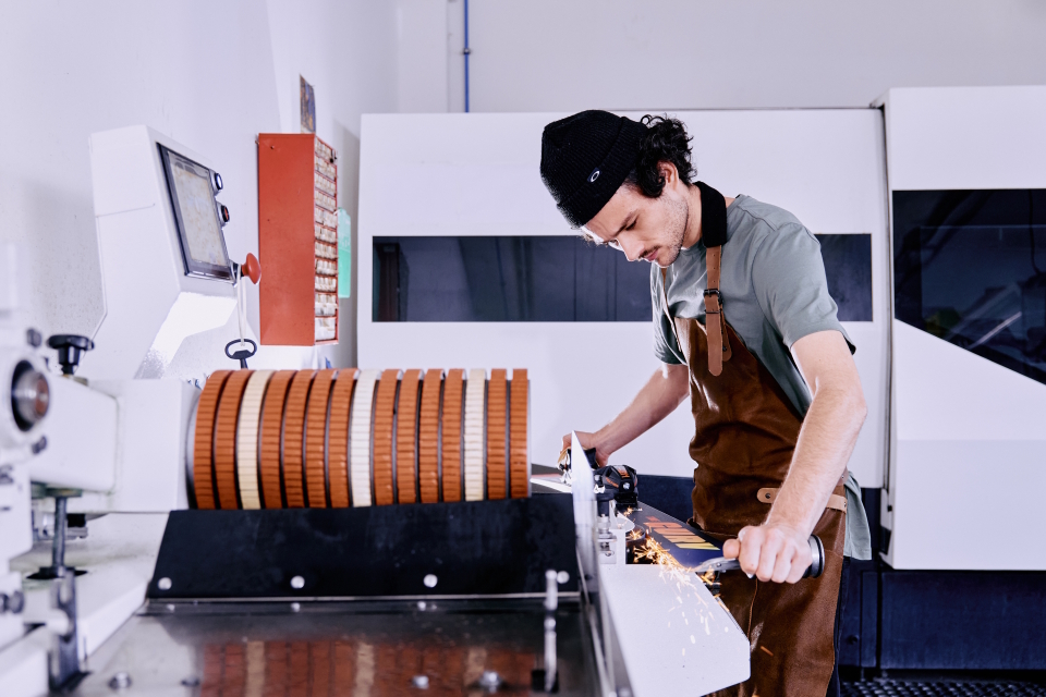 A service employee concentrates on grinding the edge of a ski on a workshop machine, sparks flying.