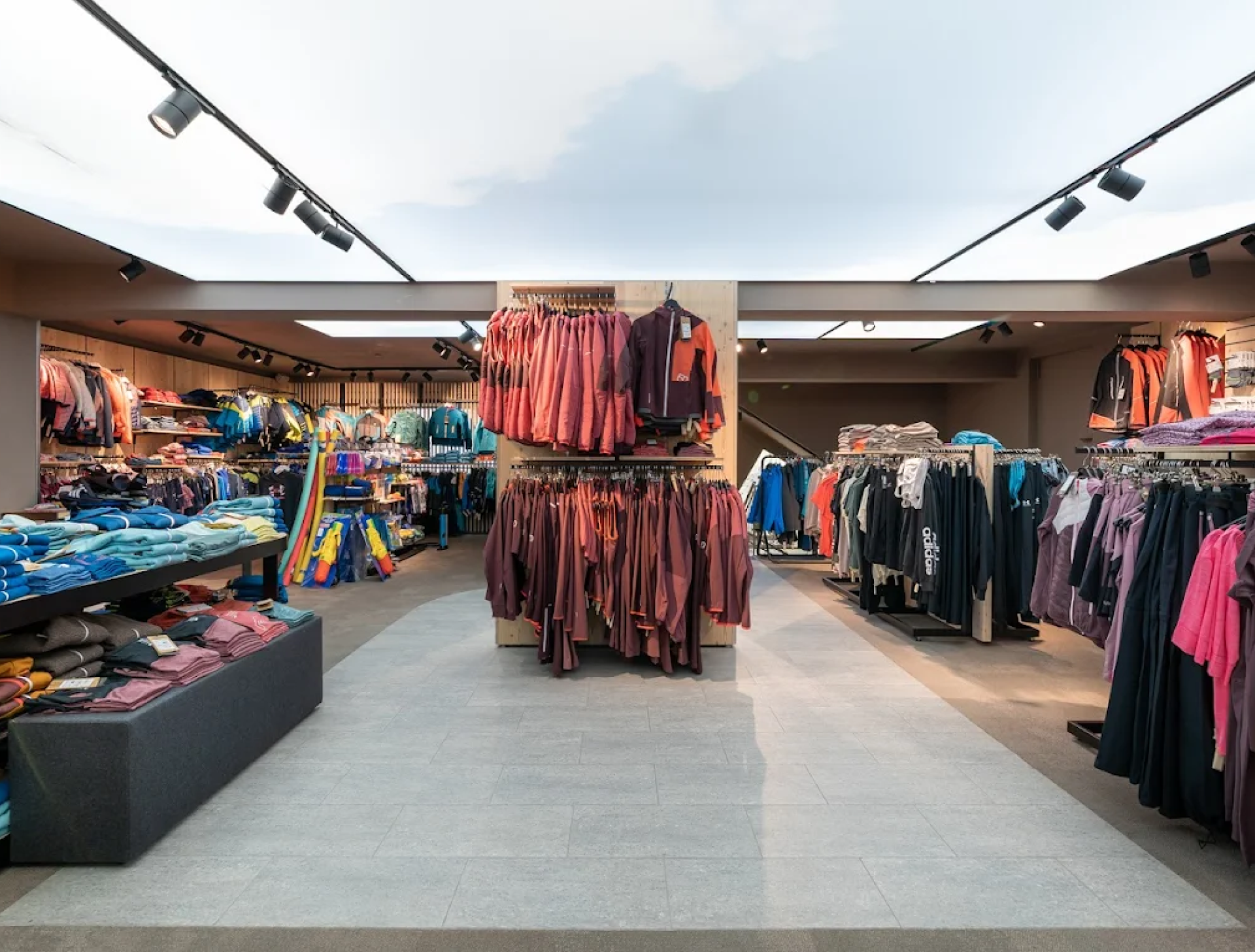 Clothing store interior featuring neatly arranged racks of colorful apparel. Bright overhead lighting creates a welcoming and organized shopping atmosphere.