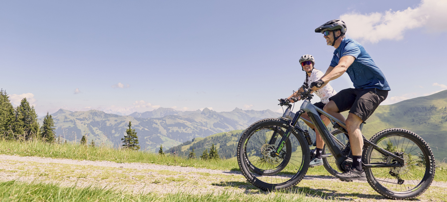 Zwei Skifahrer fahren an einem sonnigen Tag in einer verschneiten Berglandschaft Ski bergab.