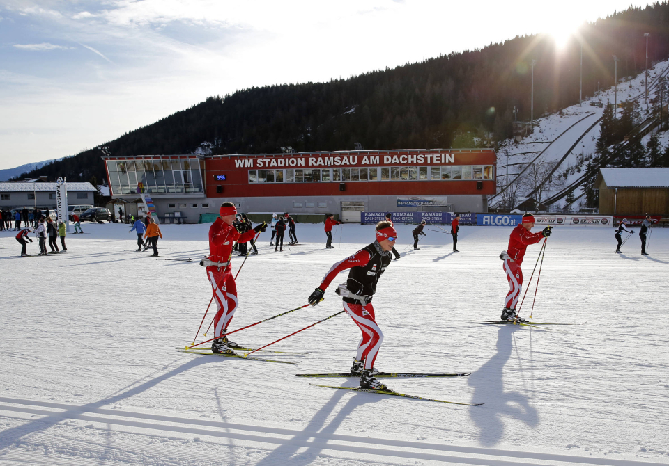 People cross-country skiing in the snow-covered practice park in Ramsau, with colorful obstacles and a sunny winter landscape.